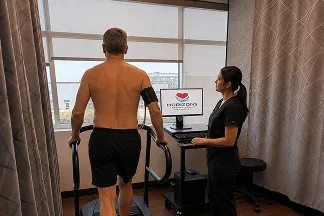 A patient walking on a treadmill during an exercise stress test while a technologist monitors